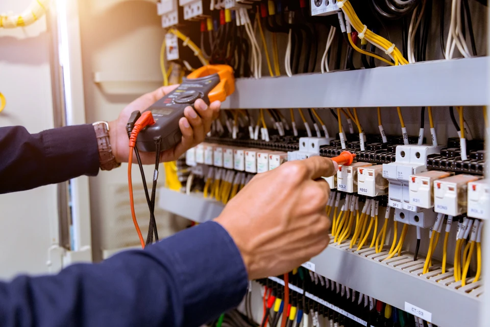 Un technicien effectue des mesures électriques sur un tableau de distribution avec un multimètre