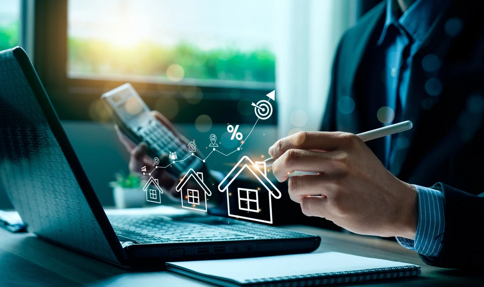 Scène d'intérieur avec professionnel utilisant ordinateur portable et smartphone, consultant données immobilières
